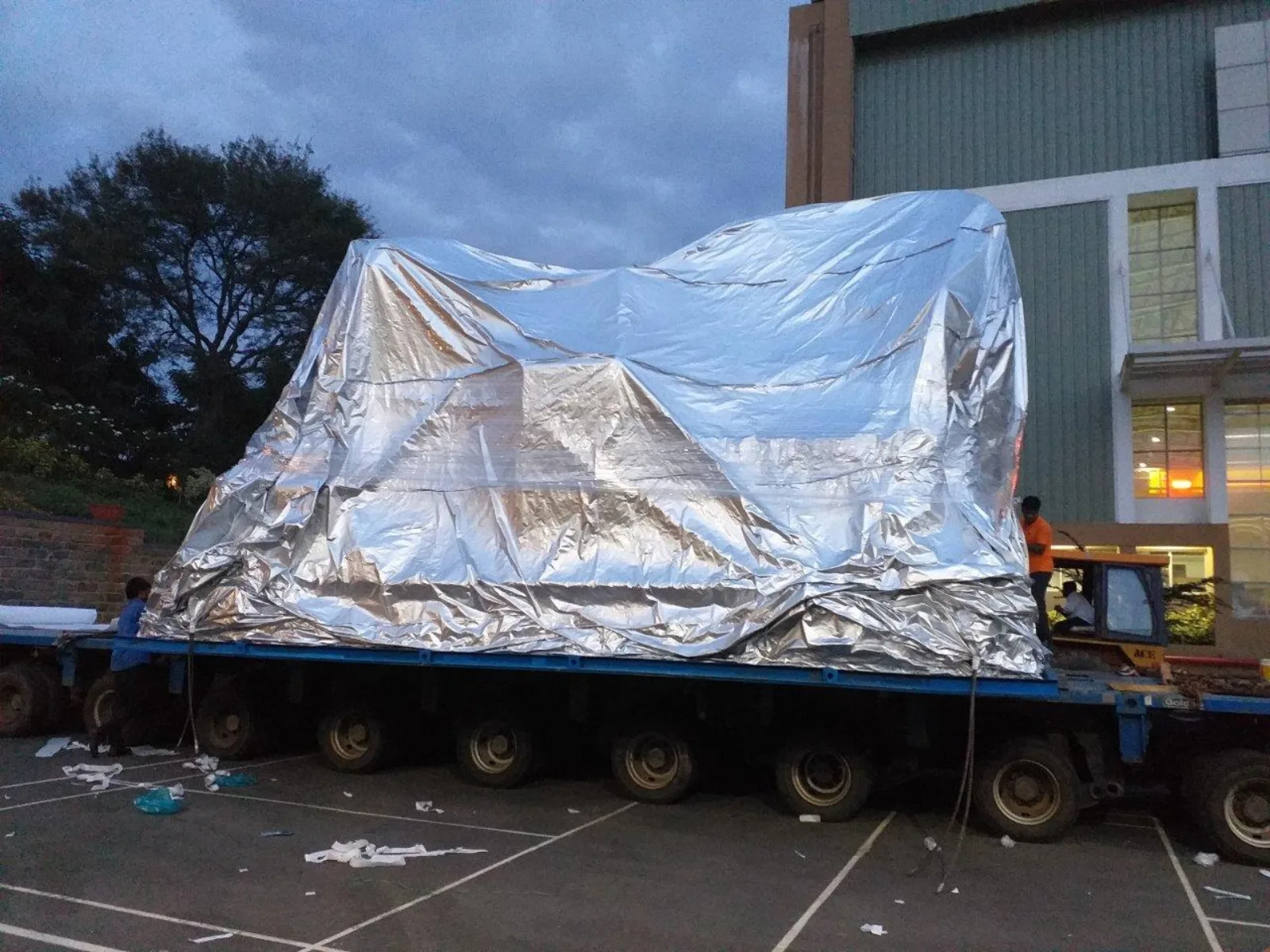 Large machine shrouded in aluminium barrier foil on a low-loader trailer